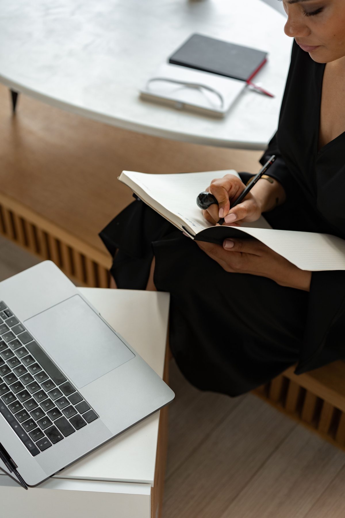 Une femme prend des notes à côté de son ordinateur portable