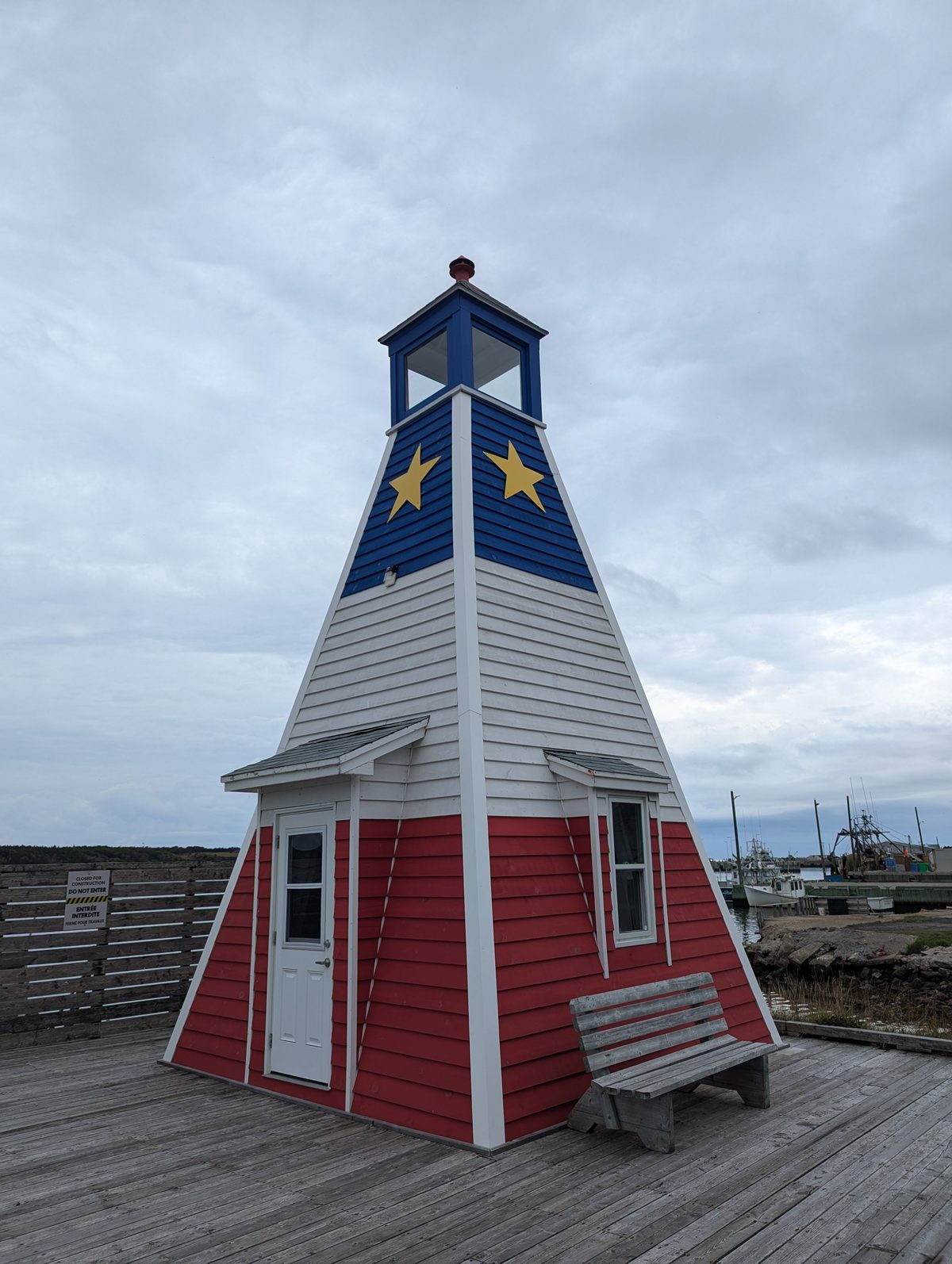 Un phare aux couleurs du drapeau acadien, sur un quai de bois