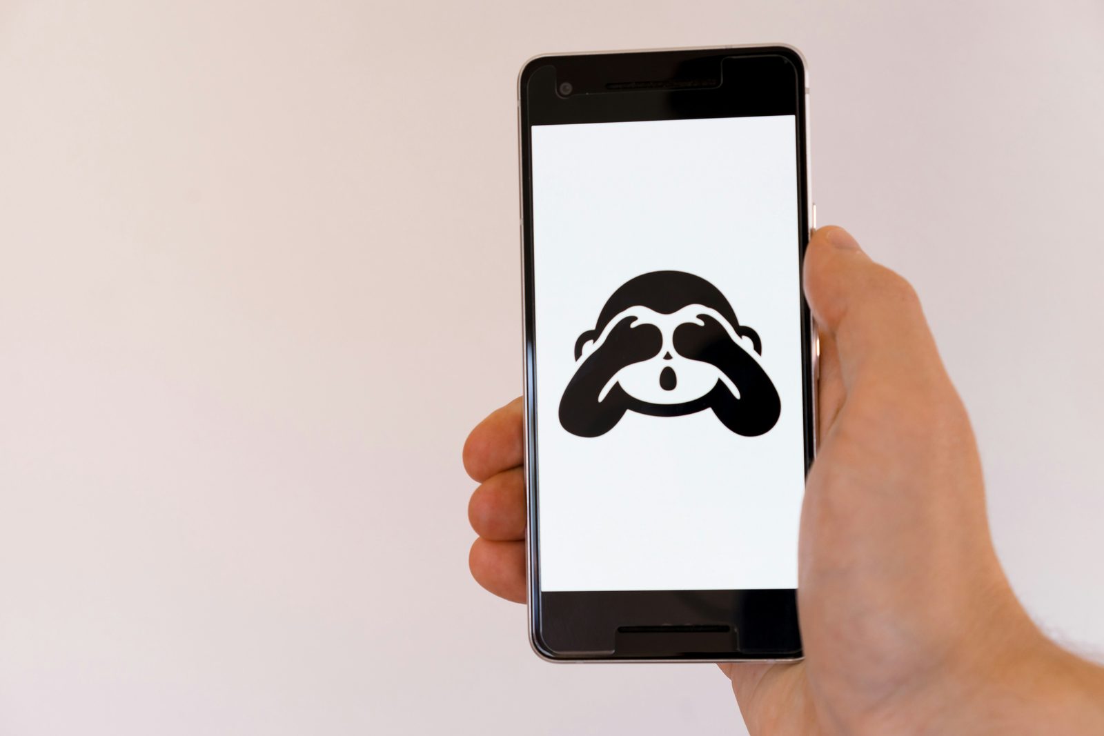 Une main tient un téléphone dont l’écran affiche l’emoji du singe qui se cache les yeux