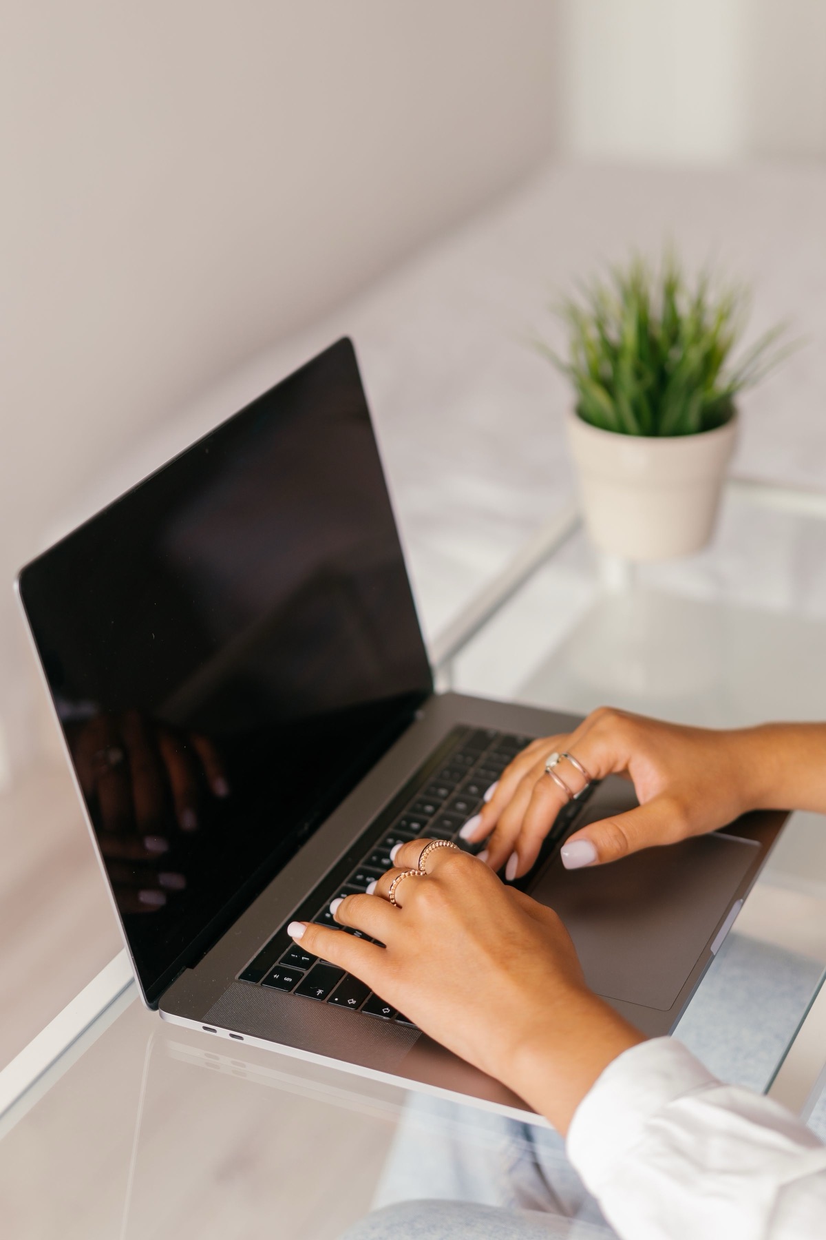 Deux mains tapent sur le clavier d’un ordinateur portable, près d’une plante verte